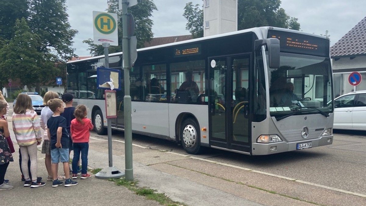 Kinder stehen an der Bushaltestelle und schauen auf einen Bus