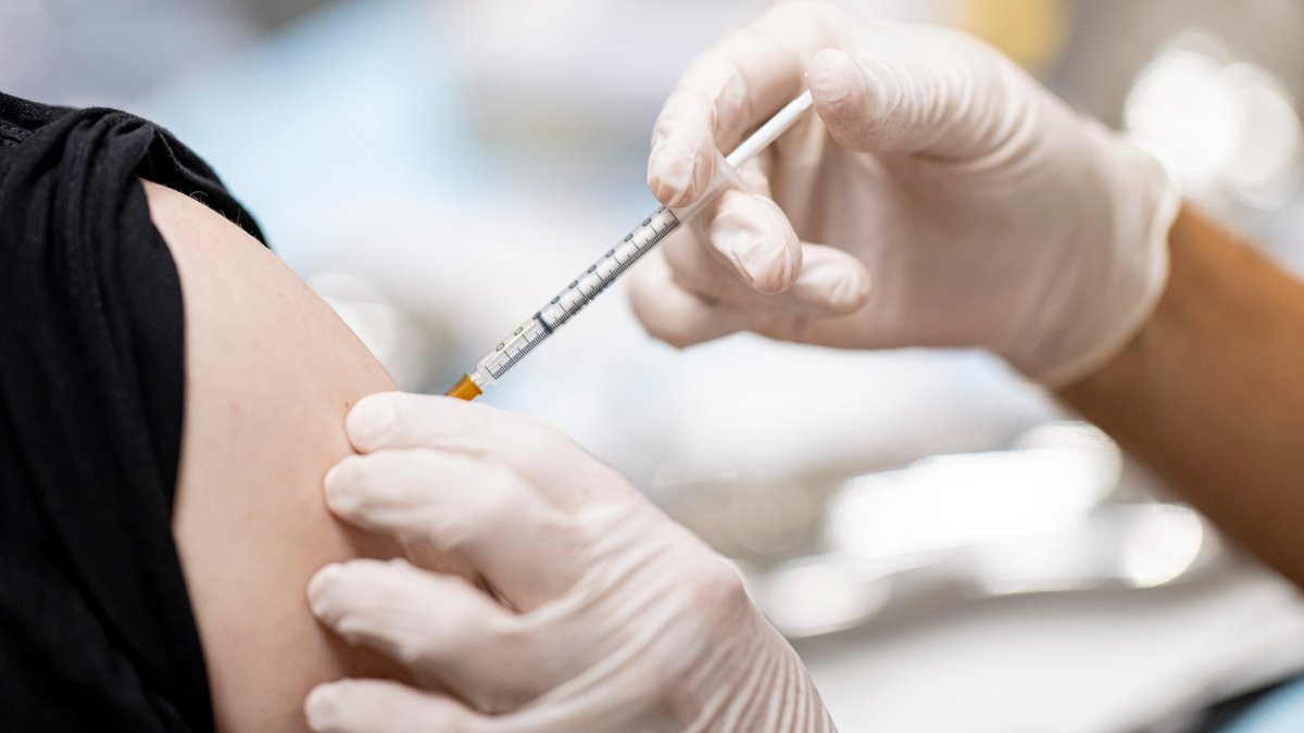 Hände in Gummihandschuhen setzen eine Spritze im Oberarm