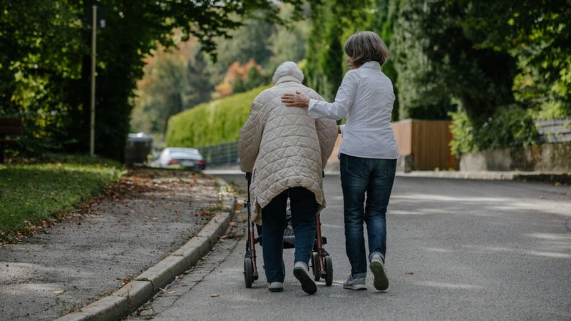 Eine Pflegerin geht mit einer Seniorin mit Rollator spazieren. | Bild: BR/Johanna Schlüter Eine Pflegerin geht mit einer Seniorin mit Rollator spazieren.