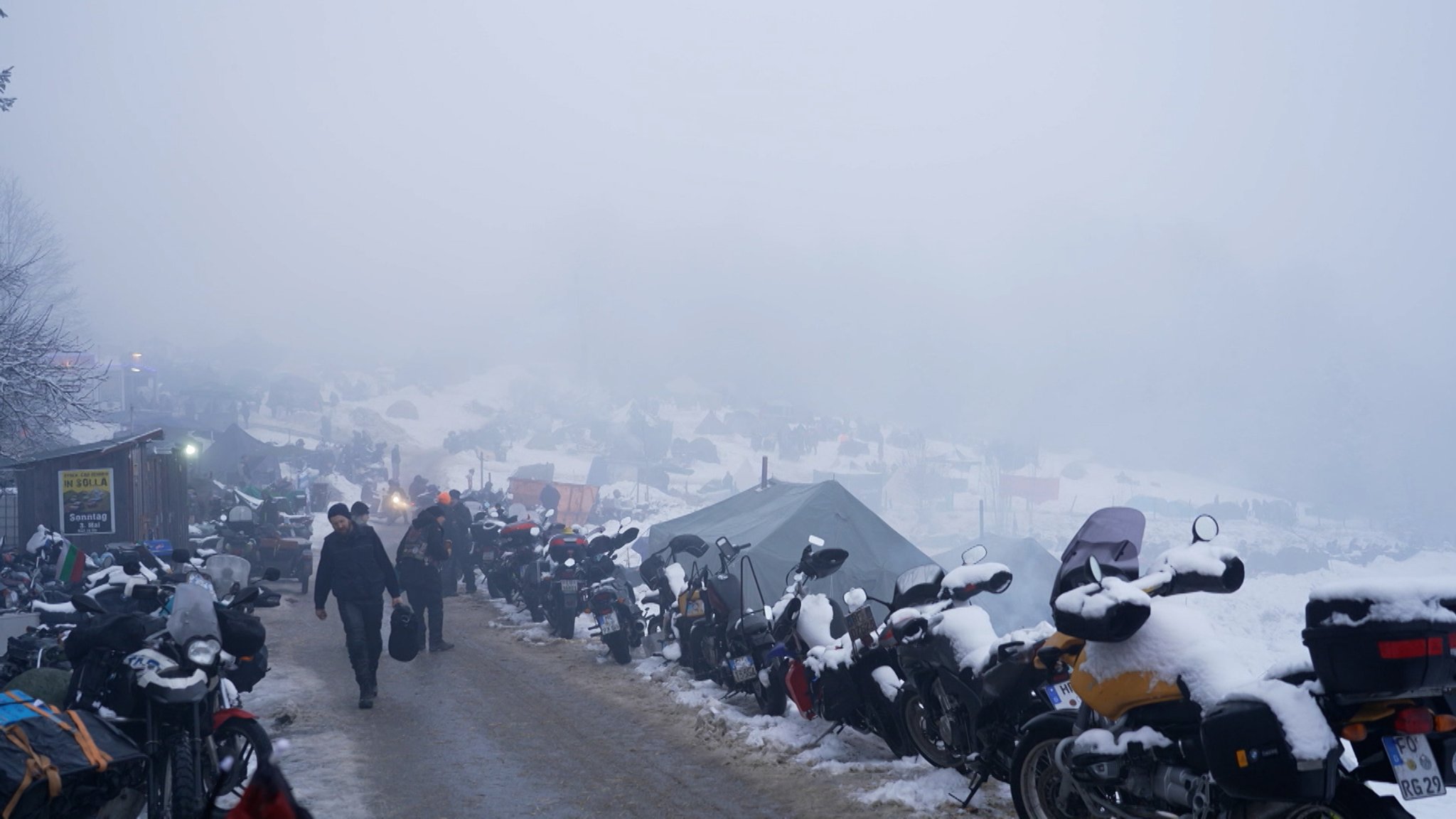 Teilnehmer gehen zu ihren verschneiten Motorrädern