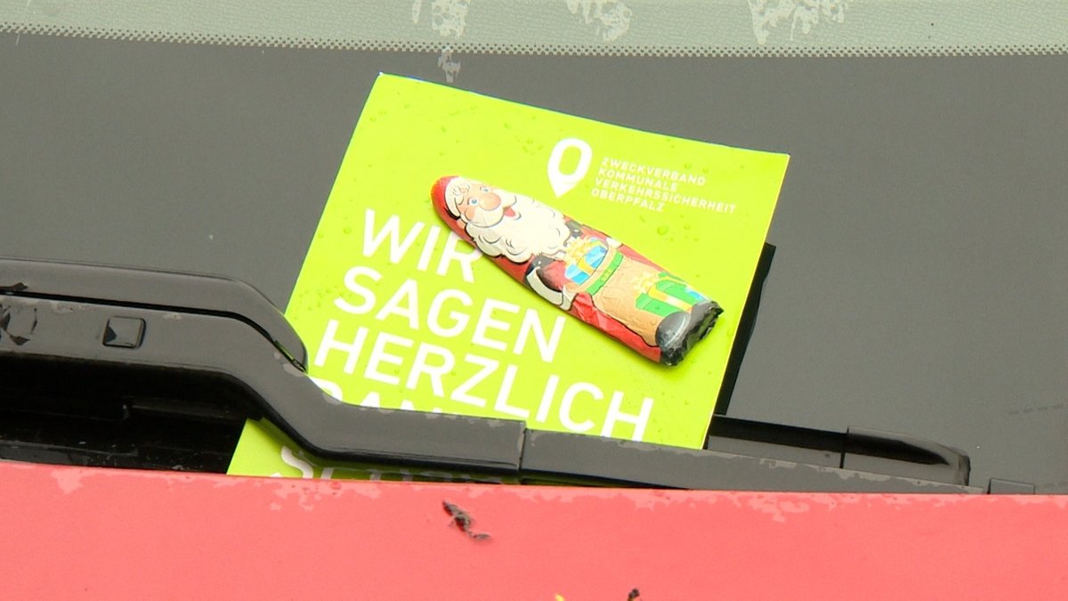 Auf der Windschutzscheibe eines Autos klemmt unter dem Scheibenwischer eine Karte mit der Aufschrift "Wir sagen herzlich Dankeschön" und einem kleinen Schokoladen-Weihnachtsmann.