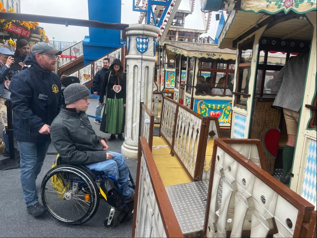 Zu sehen ist ein Mensch im Rollstuhl, der über eine Rampe in eine Gondel des Riesenrads fährt.