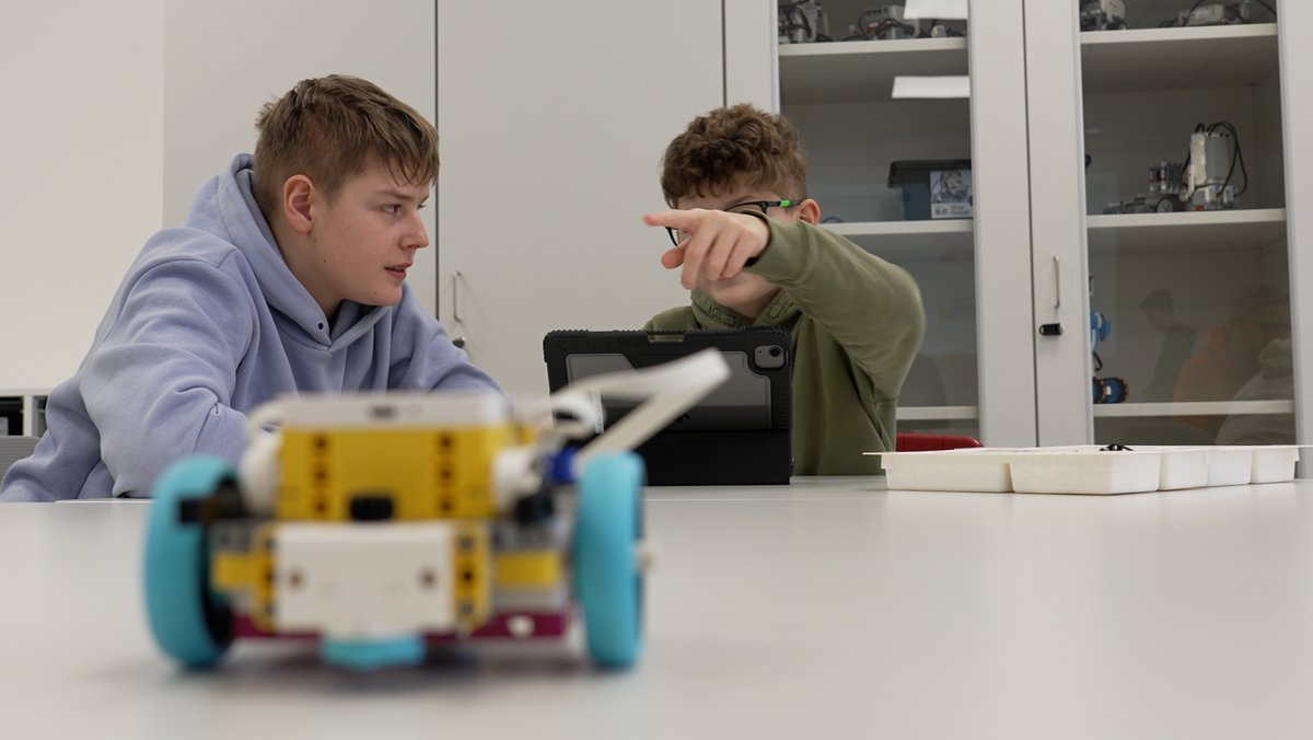 Niklas (l.) und Thomas aus der achten Klasse der Realschule am Maristenkolleg lassen einen Roboter über den Tisch fahren.