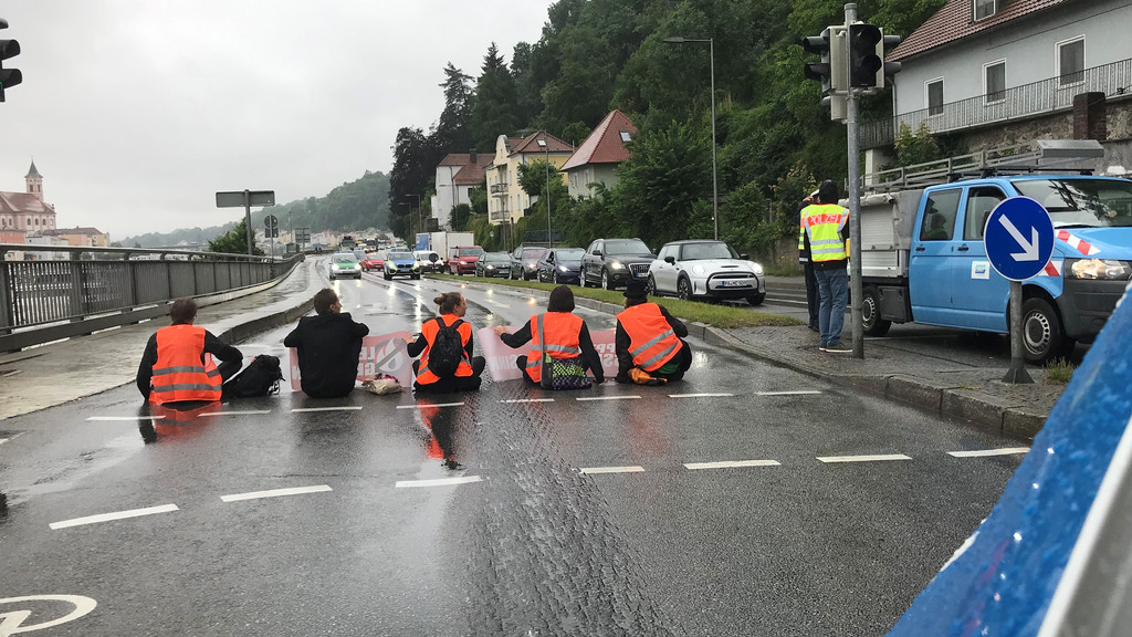 Klimaaktivisten sitzen auf der Angerstraße in Passau. Die Polizei regelt den Verkehr.