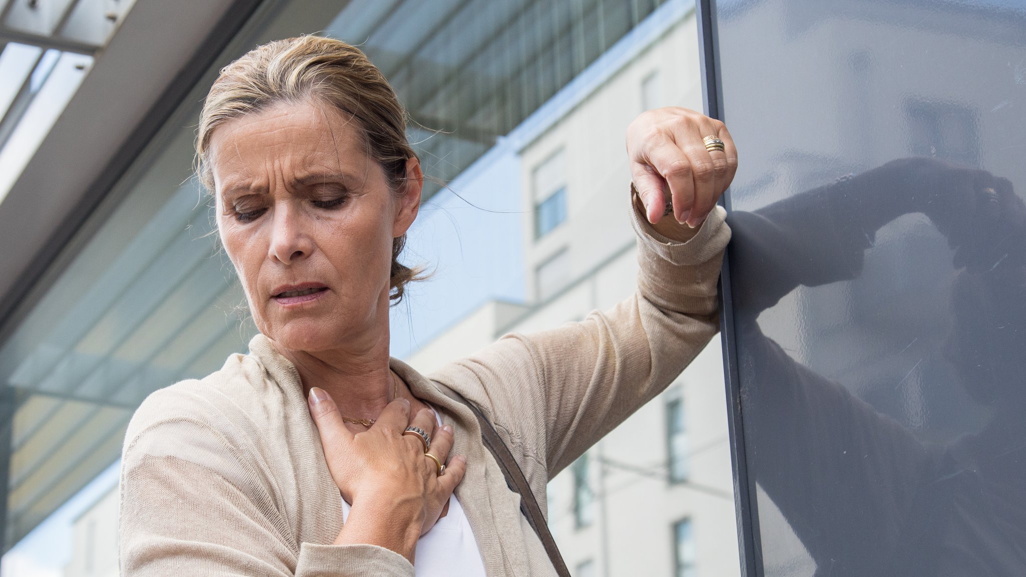 Frau mit Atemnot hält sich die Hand auf die Brust - Symbolbild