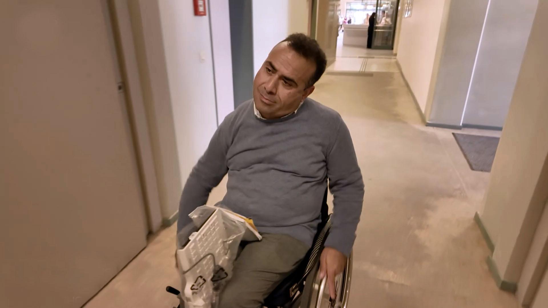 Ein Mann fährt mit Rollstuhl durch den Gang eines Amtes.