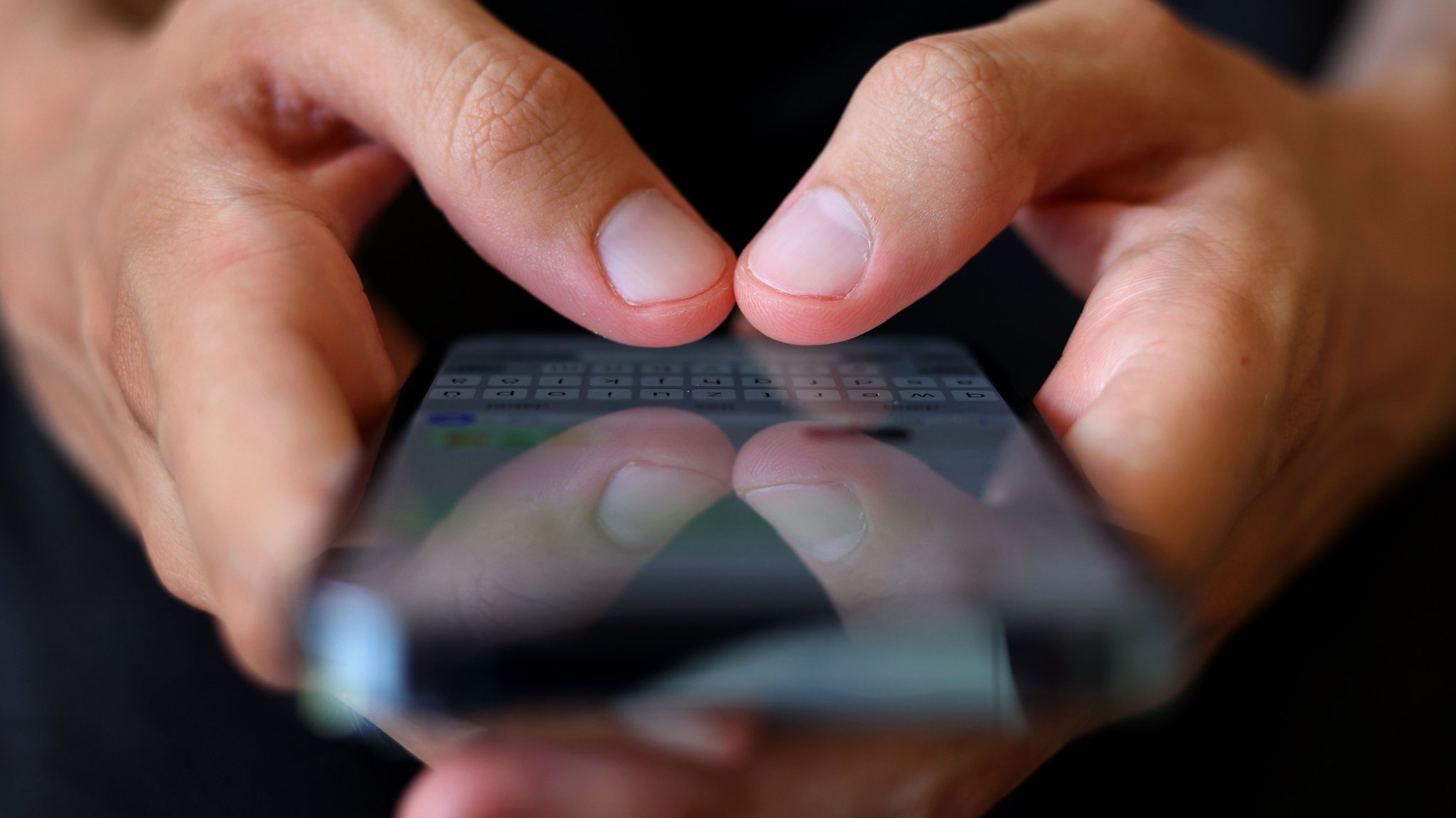 Ein Mann hält ein Smartphone mit beiden Händen und tippt eine Nachricht.