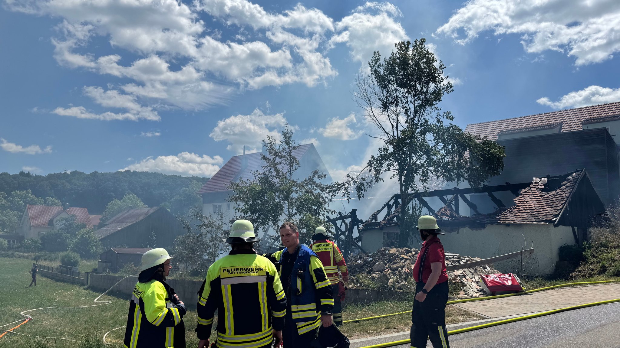 Feuerwehrleute vor der rauchenden Brandruine, ein Nebengebäude