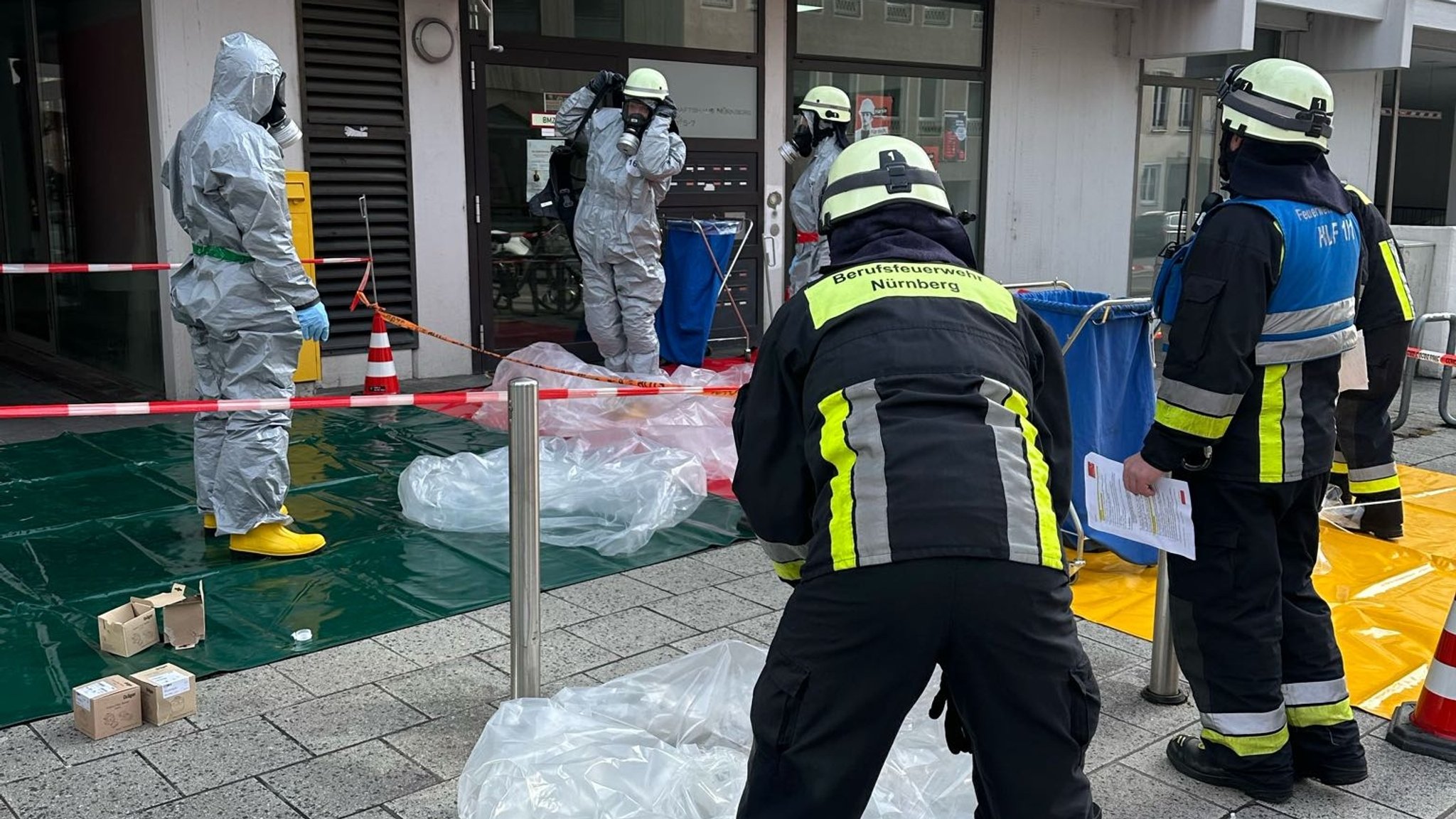 Feuerwehrmänner mit Atemschutzgerät hantieren mit Plastikplanen vor einem Gebäude. 