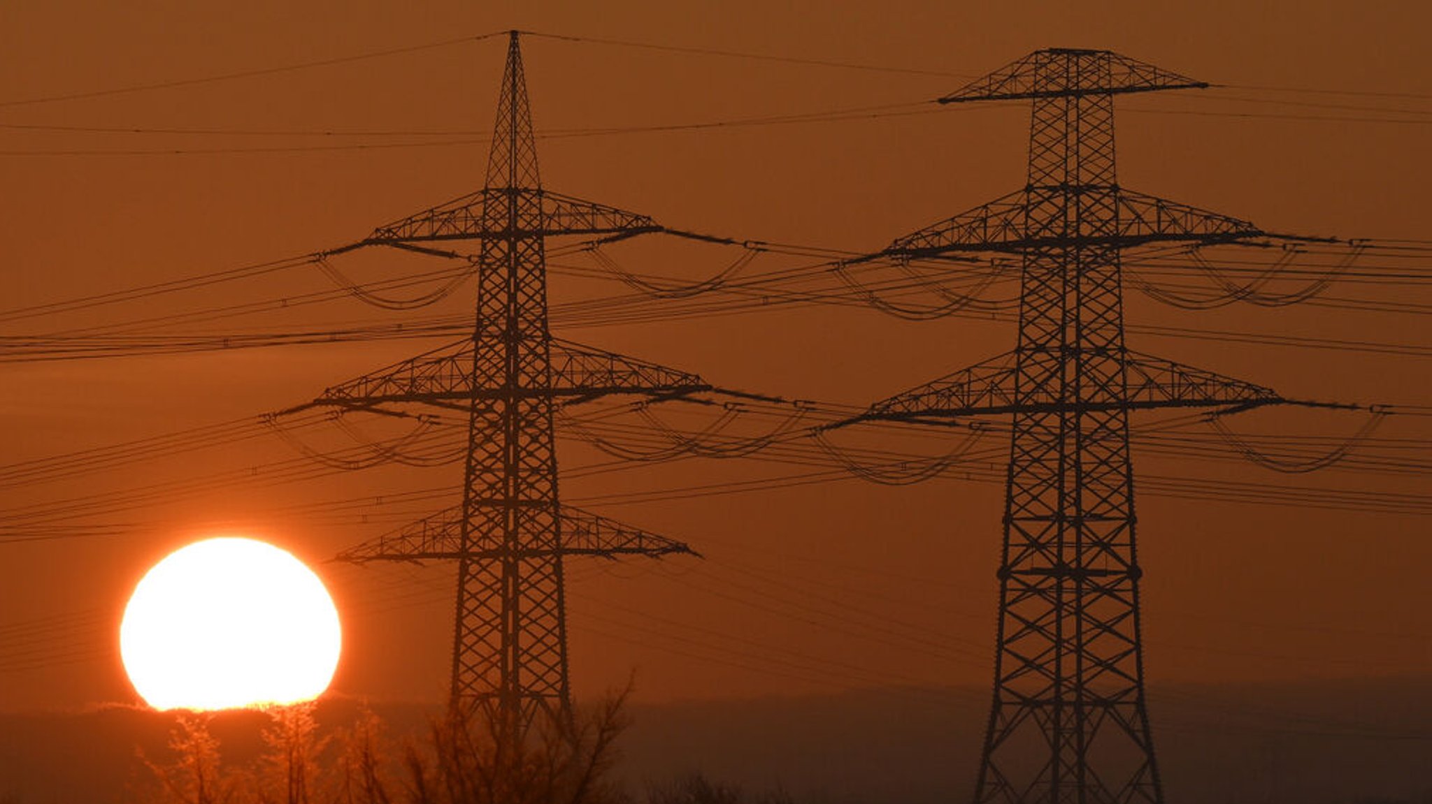 Die Sonne geht hinter Strommasten auf. (Symbolbild)