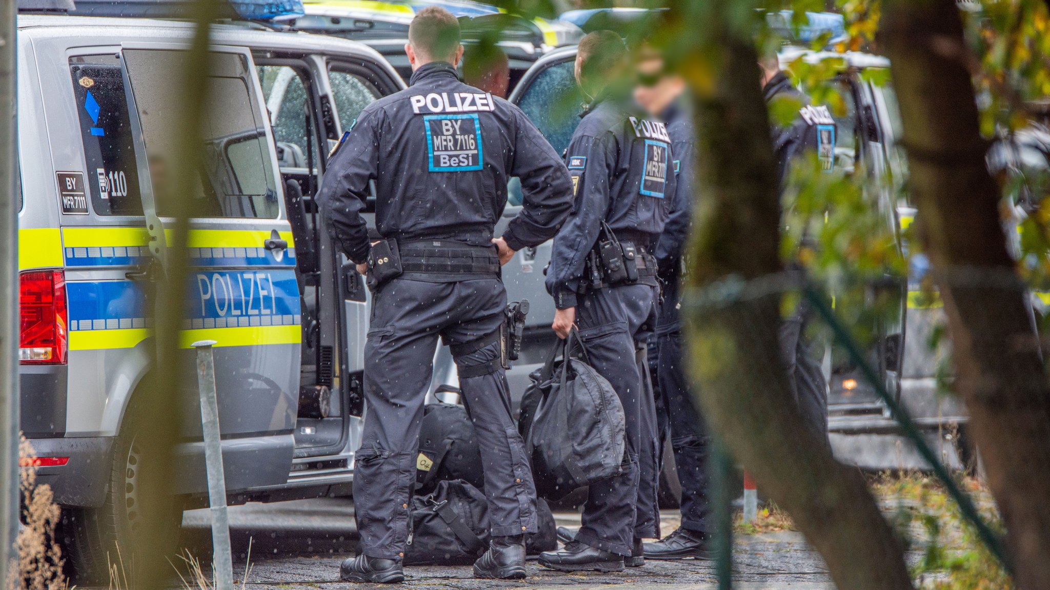 Polizisten in Uniform stehen neben Polizei-Einsatzwagen.