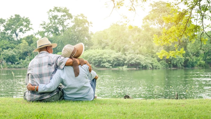 Ein älteres Paar sitzt eng umschlungen auf einer Wiese am Ufer eines ruhigen Sees. Eine Studie zeigt, dass gemeinsam erlebte Freude das Stresshormon Cortisol senkt und damit gesundheitsfördernd ist. | Bild: stock.adobe.com/SUPERMAO Ein älteres Paar sitzt eng umschlungen auf einer Wiese am Ufer eines ruhigen Sees. Eine Studie zeigt, dass gemeinsam erlebte Freude das Stresshormon Cortisol senkt und damit gesundheitsfördernd ist.