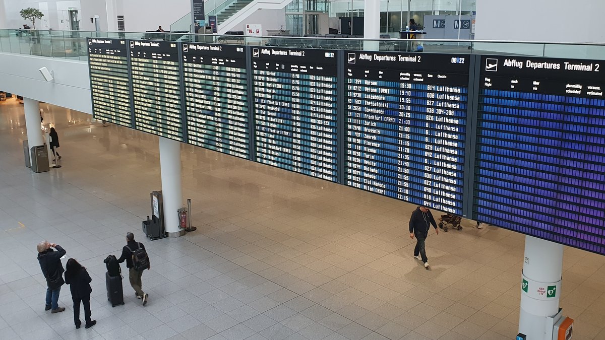 Menschen schauen auf die Anzeigetafel am Münchner Flughafen (13.3.2024).