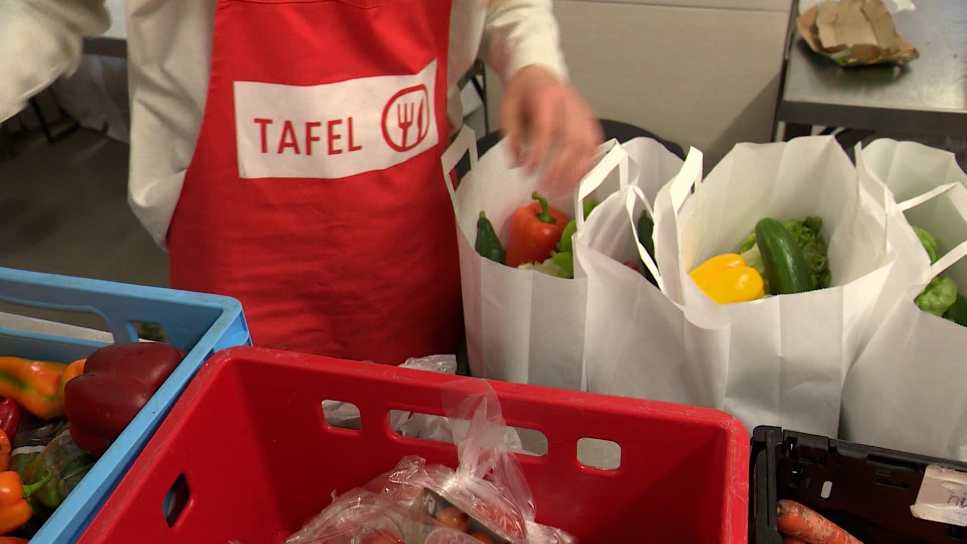 Eine helfende Person einer Tafel packt Essen in Tüten ab.
