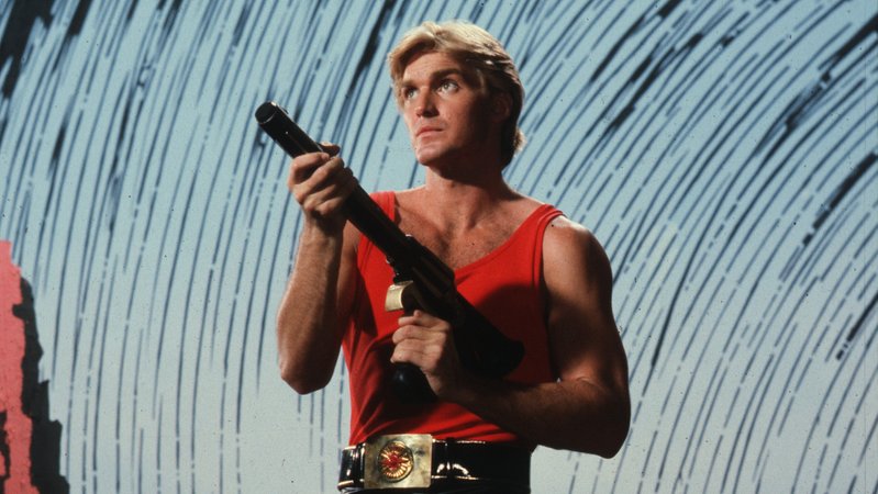 Ein Mann in rotem Heldenoutfit mit Waffe in der Hand: Szene aus "Flash Gordon 4k Remastered"