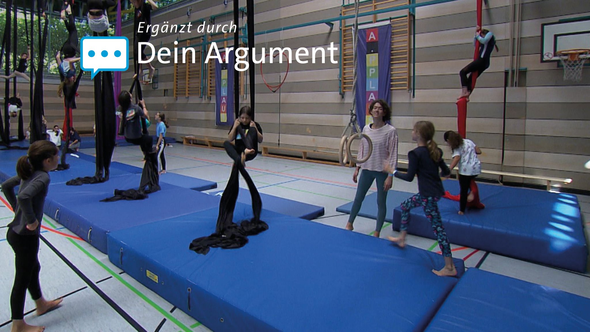 Kinder lernen in Turnhalle an von der Decke herabhängenden Tüchern Tuchakrobatik.