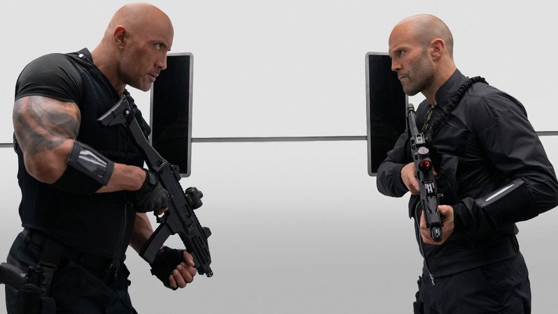 Filmszene aus "Fast & Furious: Hobbs & Shaw": Die Schauspieler Dwayne Johnson und Jason Statham stehen sich bewaffnet und schwarz gekleidet gegenüber und starren sich in die Augen.