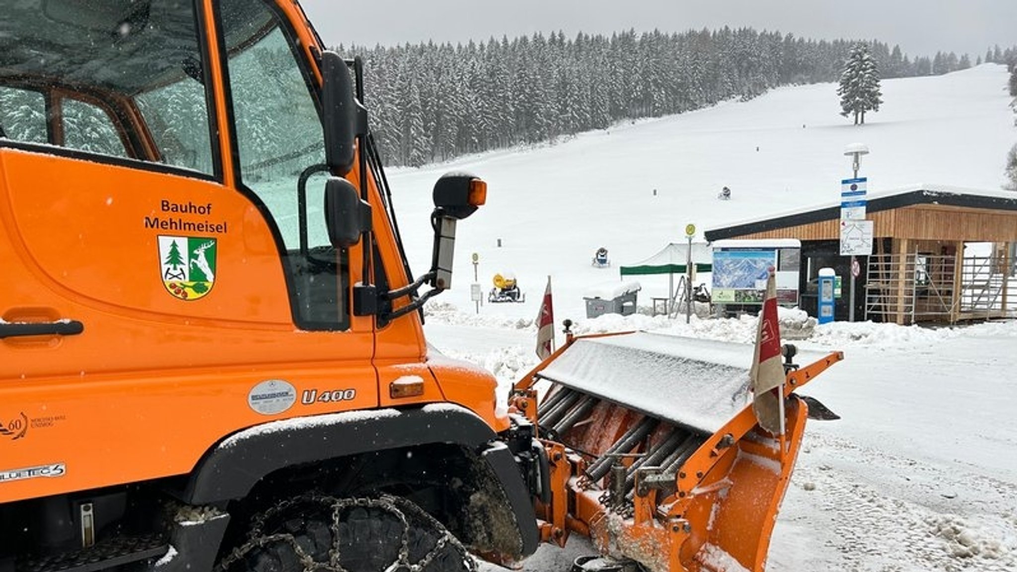 Ein Schneepflug steht an einem verschneiten Hang, dahinter ein Skilift.