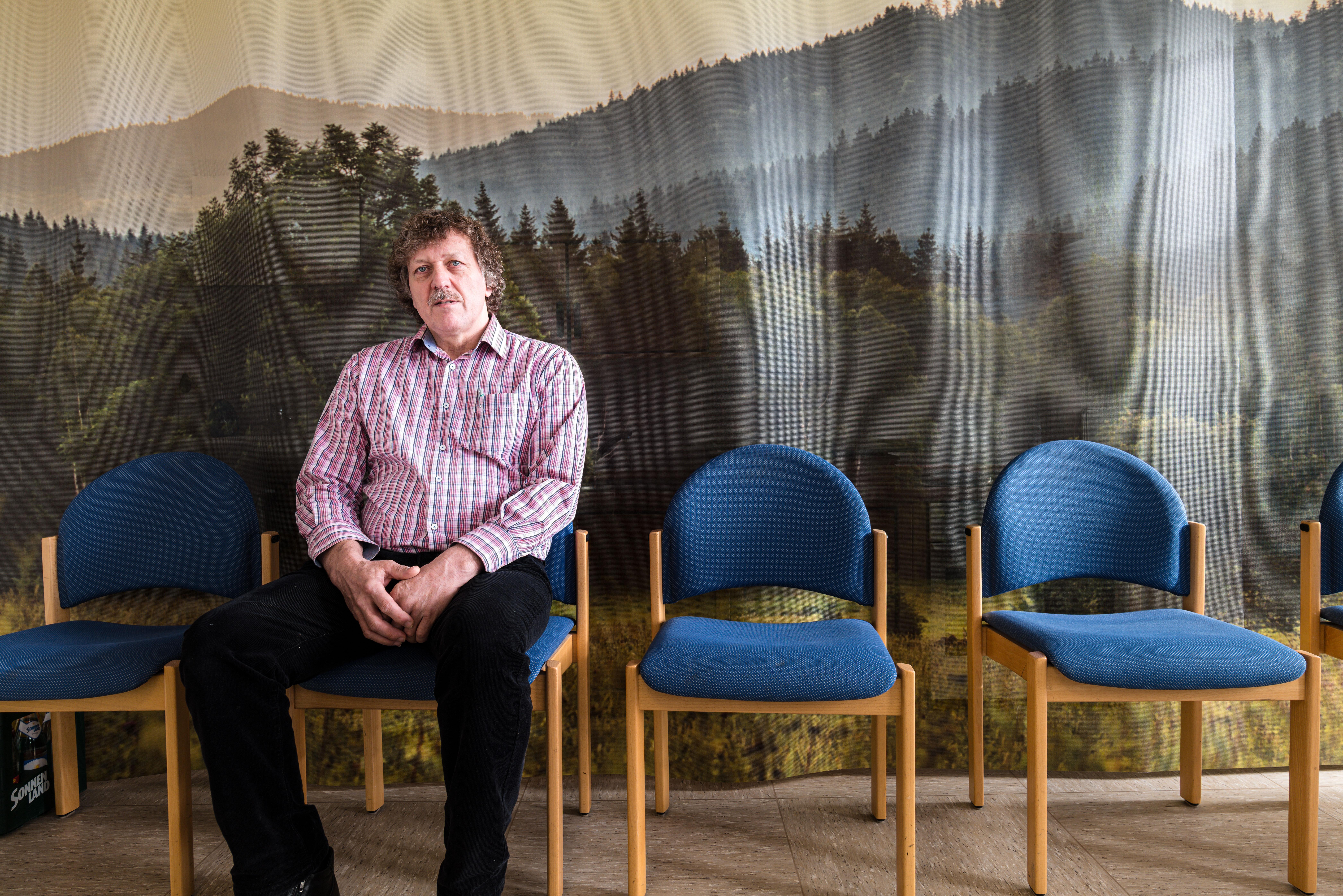 Helmut Knaus sitzt auf einem Stuhl, hinter ihm eine Wald-Tapete.