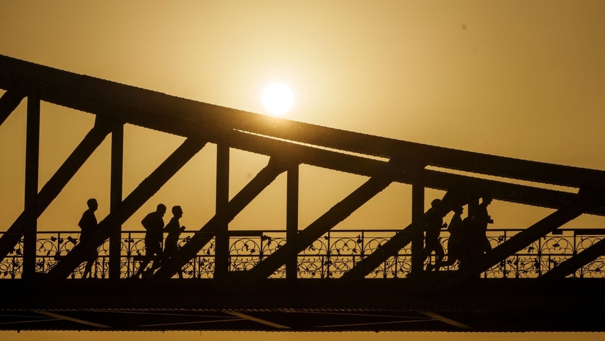 Eine Gruppe joggt bei Sonnenaufgang über den Eisernen Steg in Frankfurt am Main (Symbolbild)