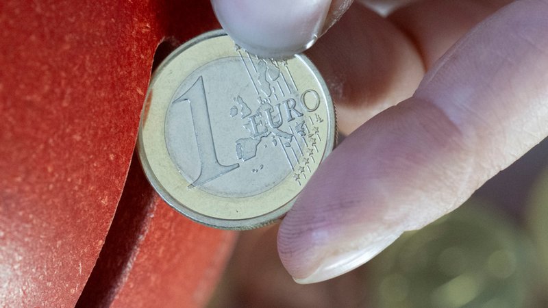 Eine Frau steckt eine 1 Euro Münze in ein Sparschwein. 