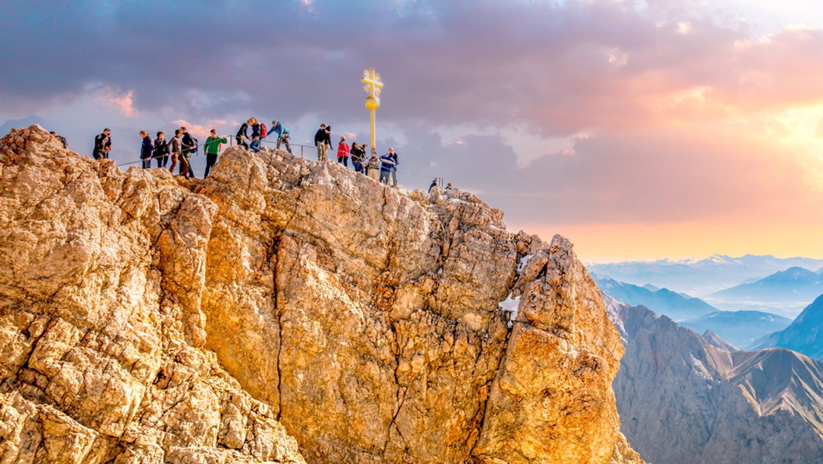 Menschen drängen sich in der Abendsonne am Gipfelkreuz der Zugspitze.