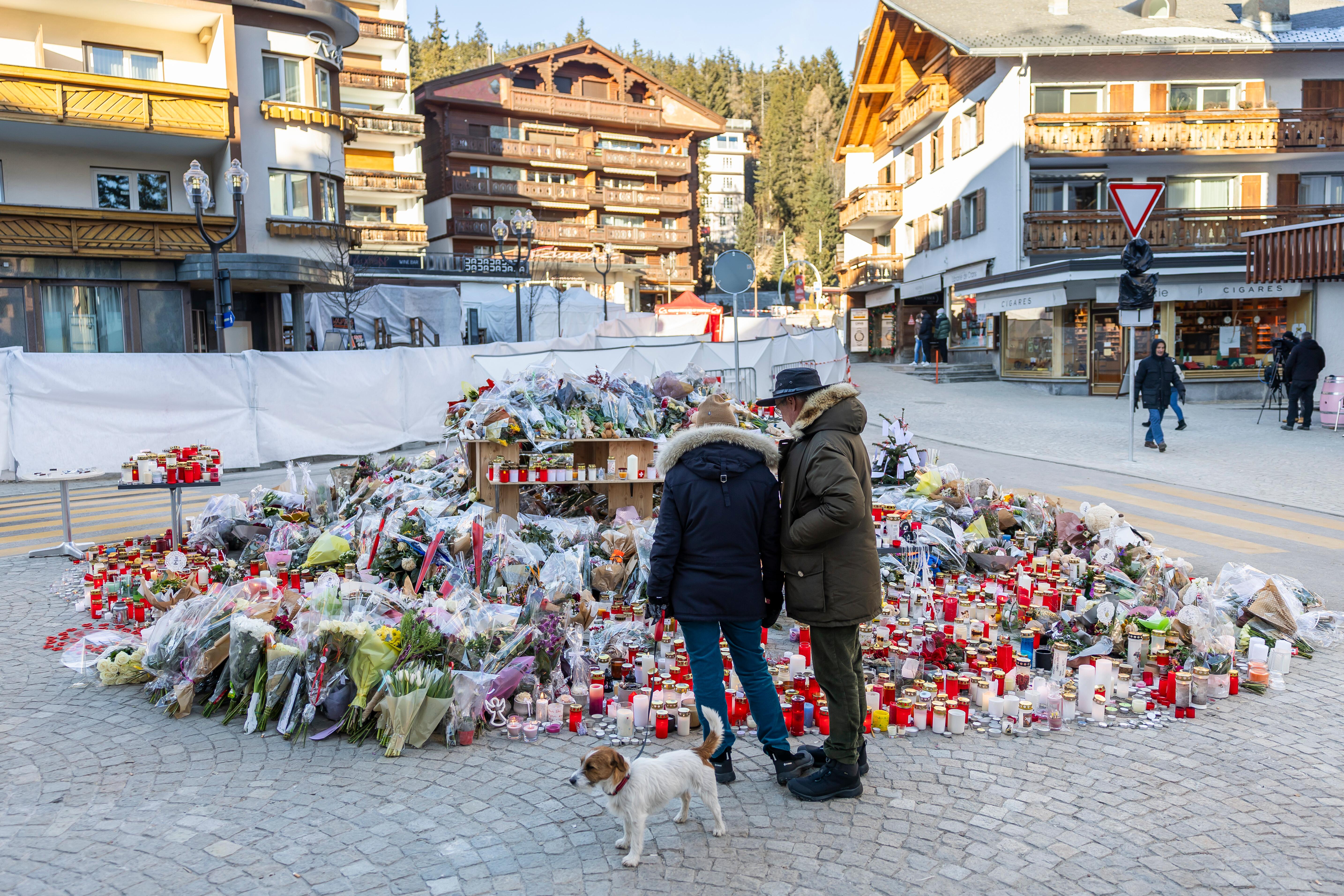 Vor Bauzäunen, die die ausgebrannte Lokalität in Crans-Montana verdecken, häufen sich Blumen und Kerzen für die Opfer der Brandkatstrophe.