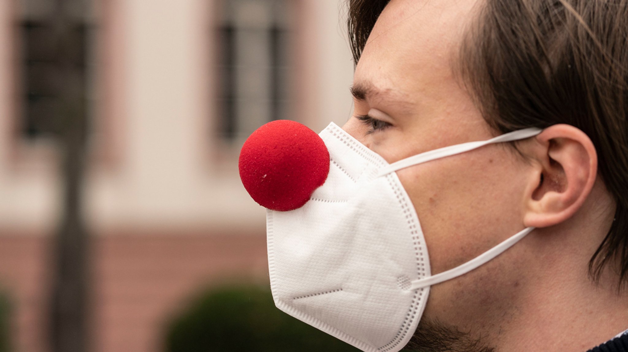 Ein junger Mann mit FFP2-Maske und einer roten Faschingsnase