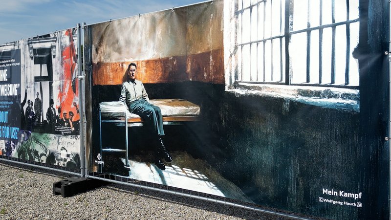 Banner mit einem Bildnis Hitlers in seiner Gefängniszelle in Landsberg, montiert an einem Bauzaun-Segment | Bild: BR / German Groß Banner mit einem Bildnis Hitlers in seiner Gefängniszelle in Landsberg, montiert an einem Bauzaun-Segment