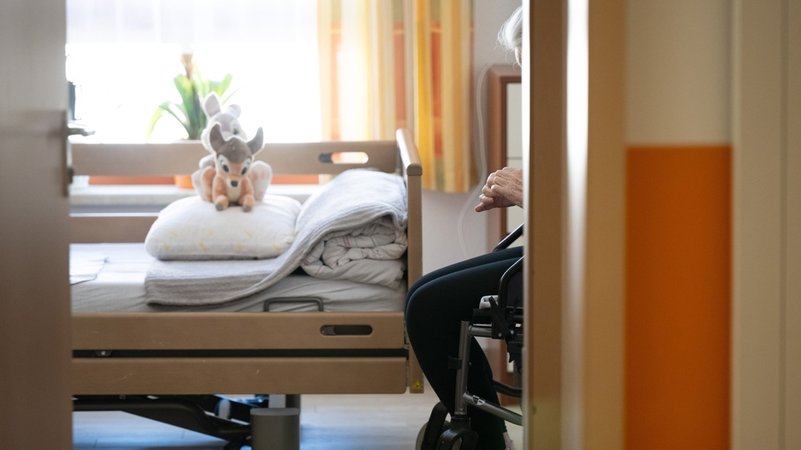 (Symbolbild) Ein Bewohner sitzt in einem Altenheim in seinem Zimmer in einem Rollstuhl. Auf dem gemachten Bett liegt ein Stofftier. | Bild: dpa-Bildfunk/Sebastian Kahnert (Symbolbild) Ein Bewohner sitzt in einem Altenheim in seinem Zimmer in einem Rollstuhl. Auf dem gemachten Bett liegt ein Stofftier.