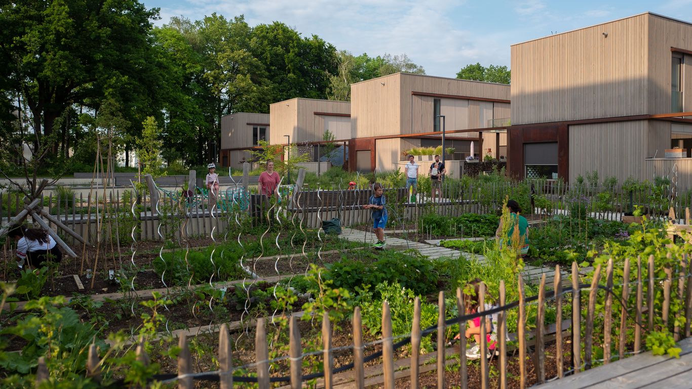 Kleine Gärten neben den Holzhäusern, außerdem sind mehrere Menschen zu sehen, die im Garten arbeiten oder draußen stehen. 