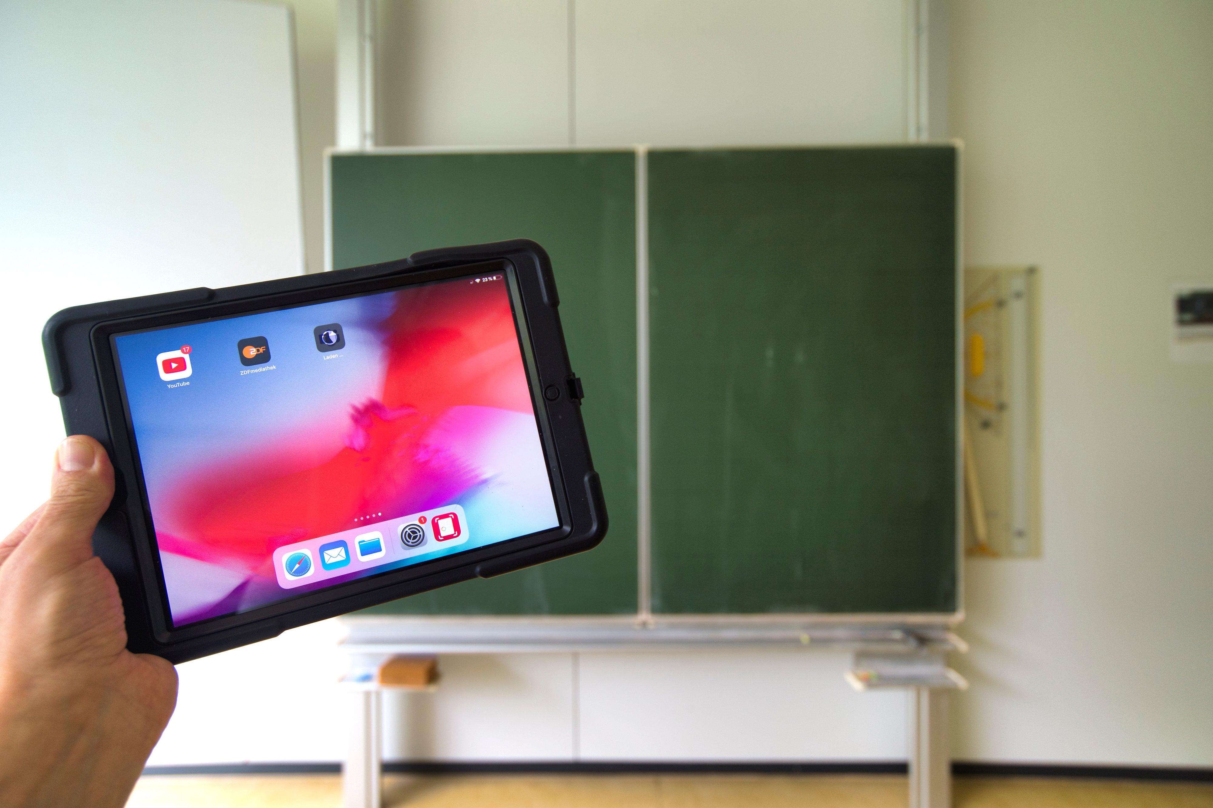 Eine hand hält einen Tablet-PC in einem Klassenzimmer hoch