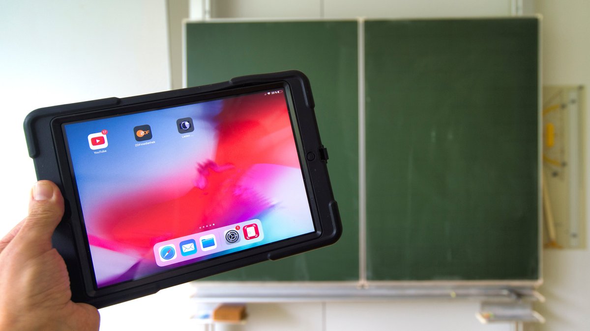 Eine hand hält einen Tablet-PC in einem Klassenzimmer hoch