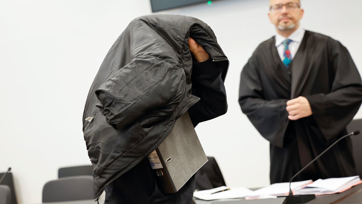 Der Angeklagte verdeckt seinen Kopf unter einer Jacke.