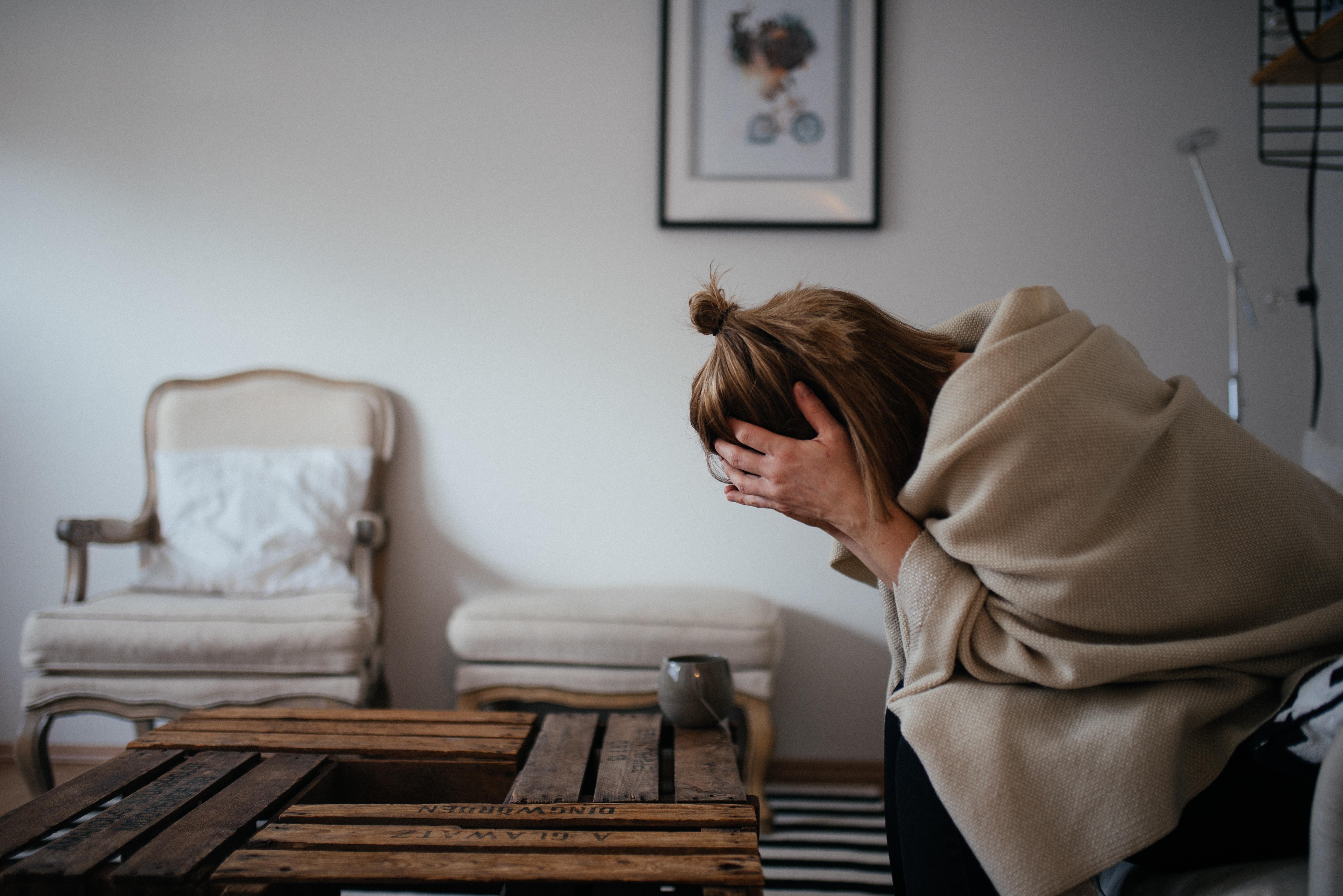 Frau sitzt im Wohnzimmer und stützt den Kopf in die Hände