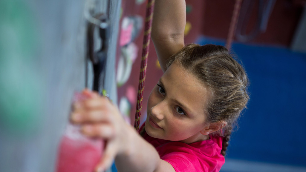Symbolbild: Entschlossenes Teenager-Mädchen, das im Fitnessstudio Klettern übt.