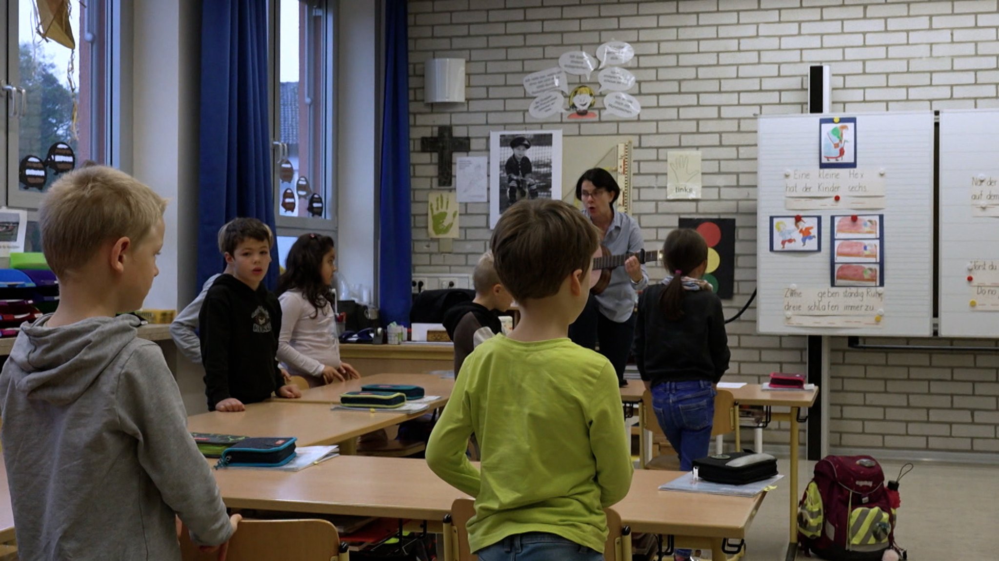 Schulkinder stehen mit einer Lehrerin in einem Klassenzimmer.