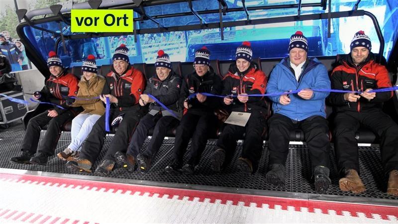 Acht Personen mit Schimützen sitzen bei der Eröffnung des neuen 8er-Sessellifts nebeneinander in den neuen Sitzen.