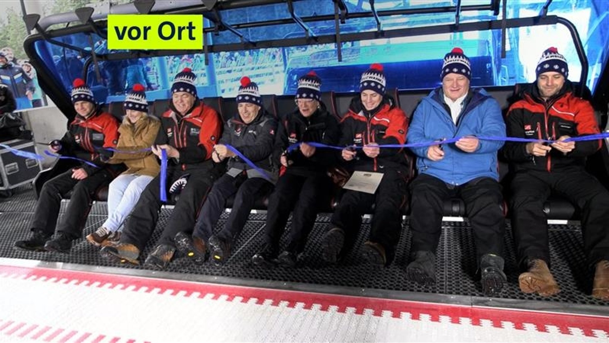 Acht Personen mit Schimützen sitzen bei der Eröffnung des neuen 8er-Sessellifts nebeneinander in den neuen Sitzen.