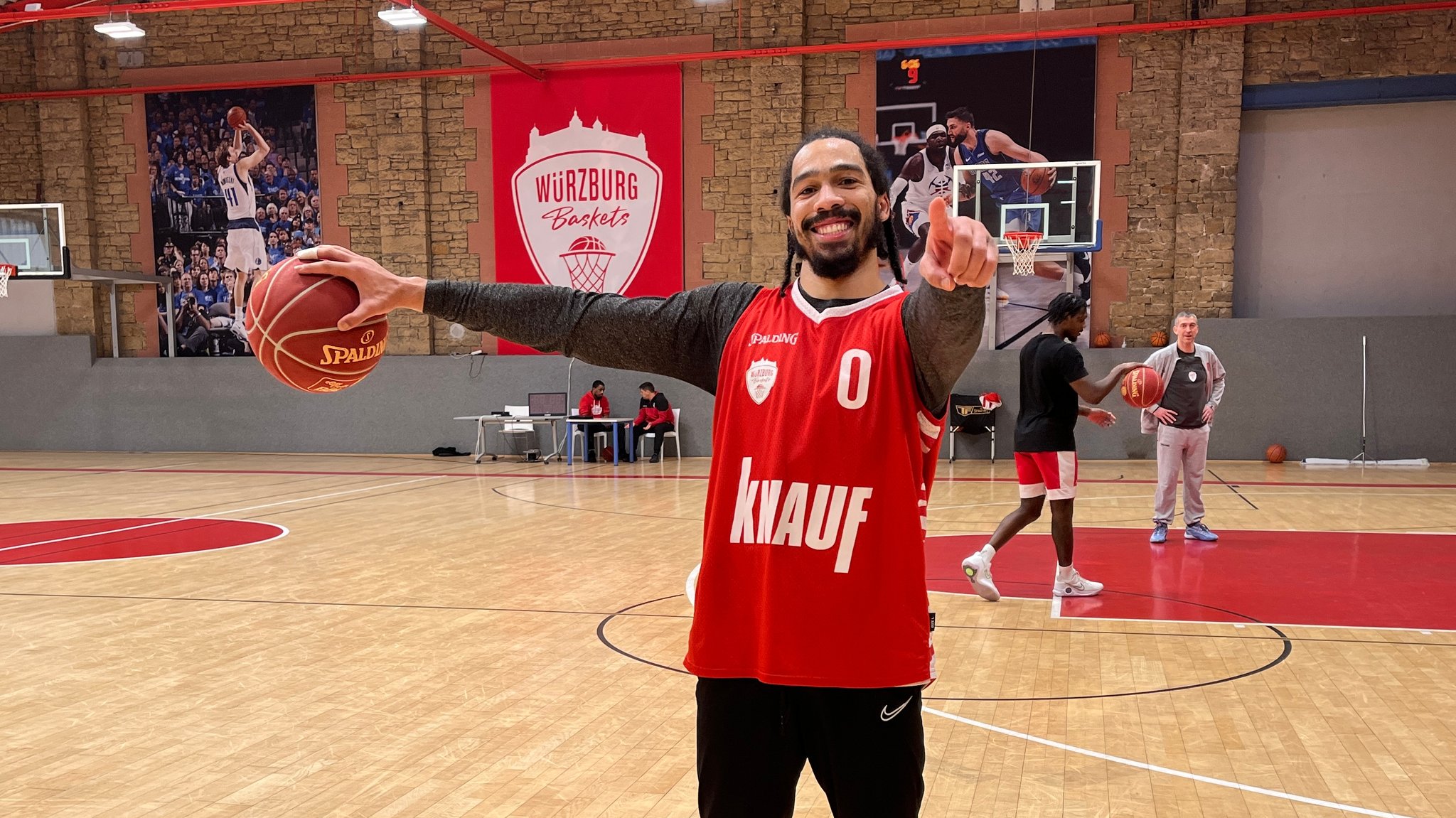 Spielmacher Otis Livingston hält einen Basketball mit einer Hand fest und zeigt in die Kamera.