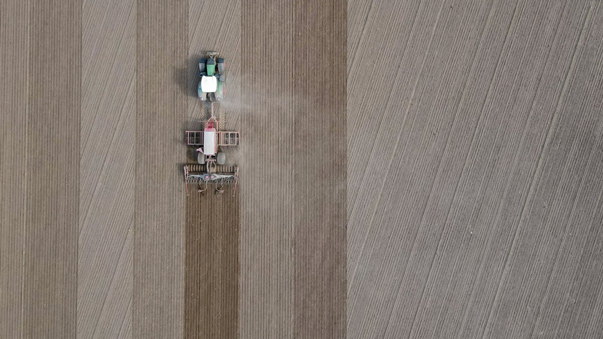 Ein Landwirt fährt mit seinem Traktor und angehängter Drille über ein Feld und bringt Saatgut in den Boden aus.