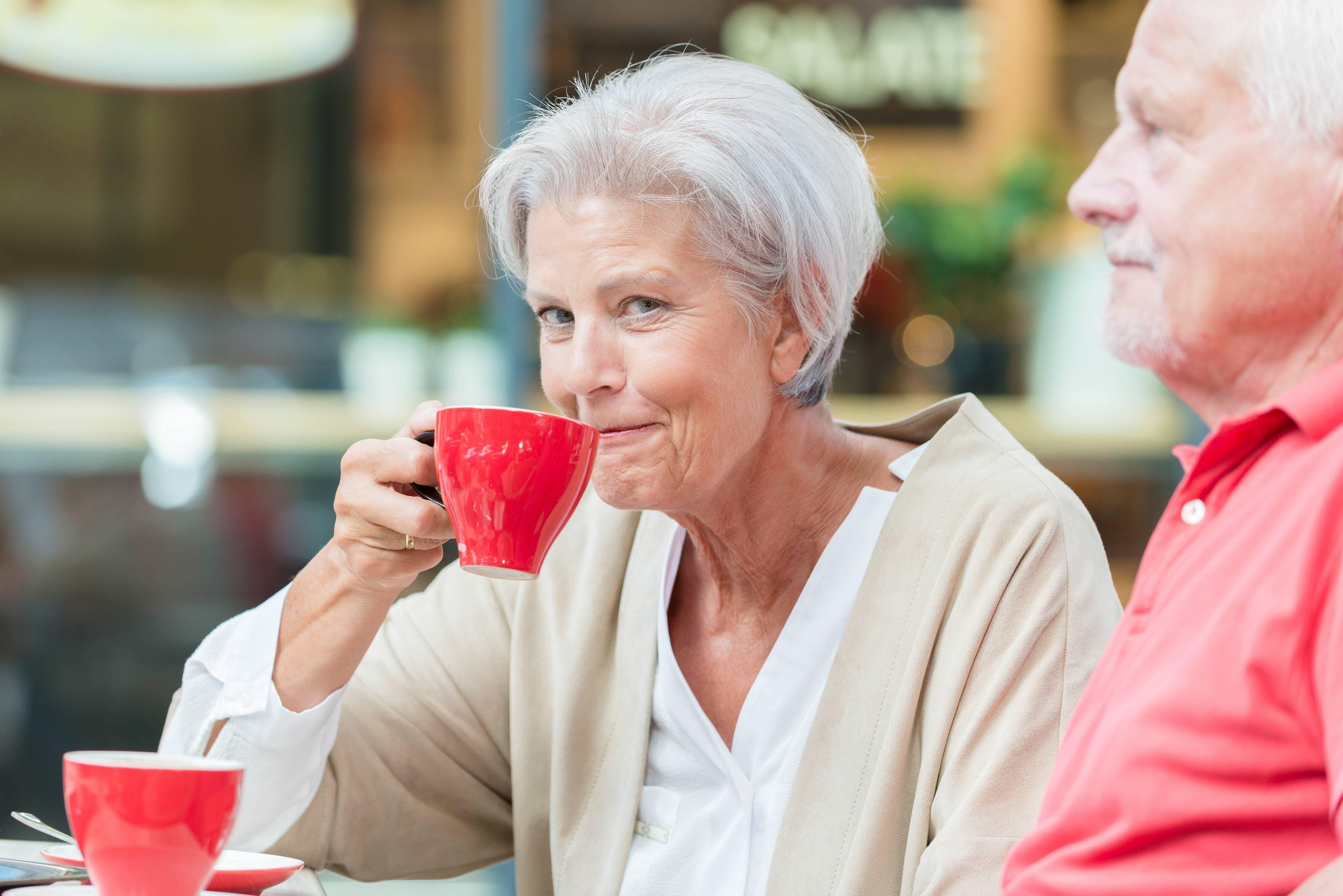 Zwei lächende Senioren sitzen in einem Cafe und trinken aus einer roten Tasse