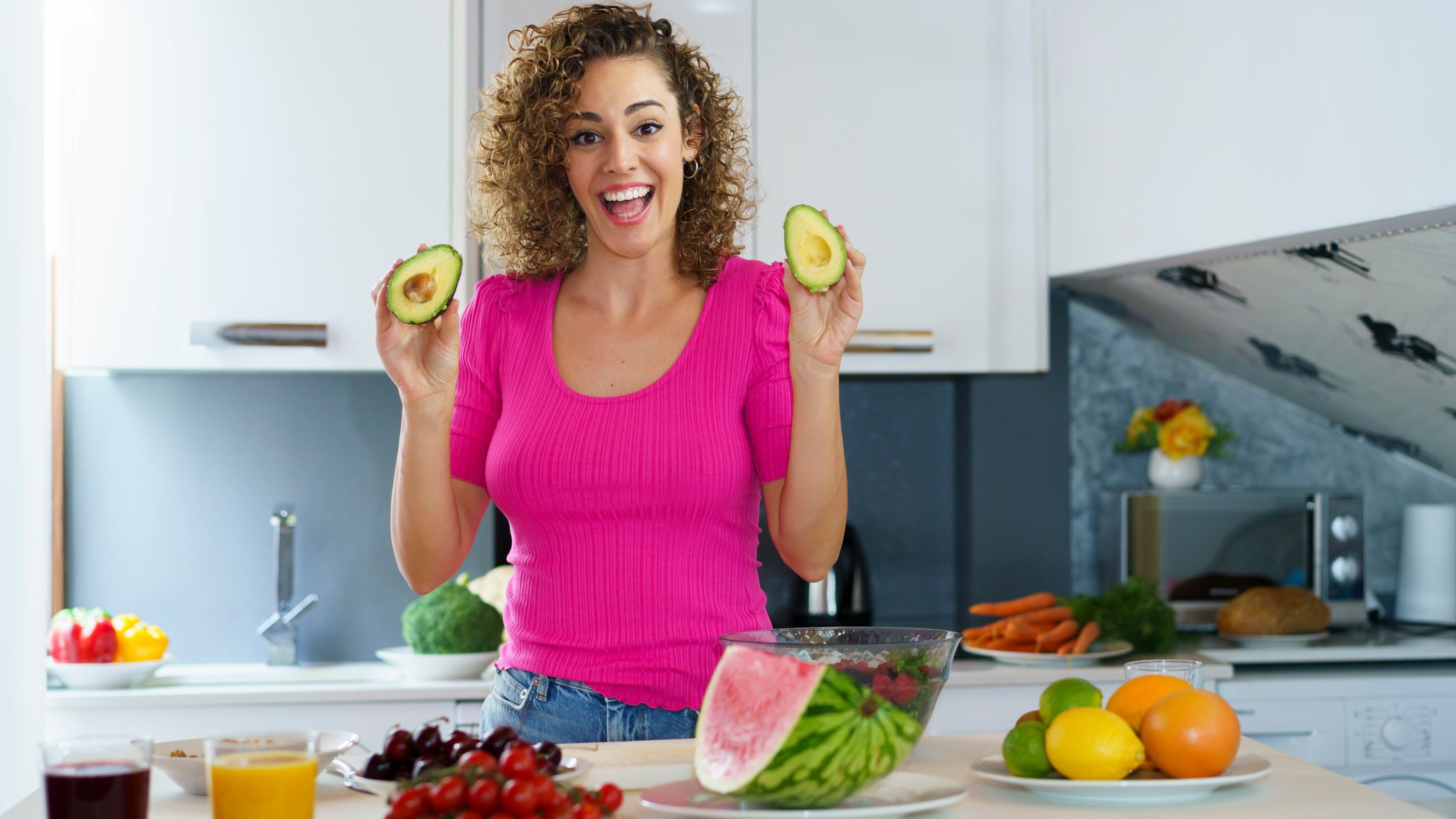 Eine lachende junge Frau hält eine aufgeschnittene Avocado in den Händen