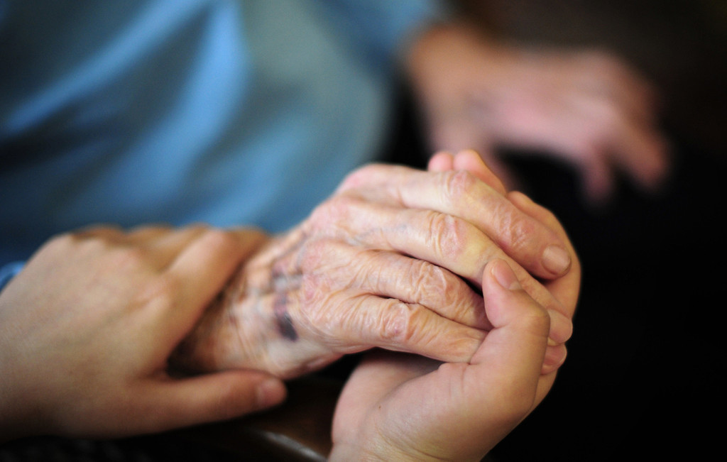 Hand einer Pflegerin hält eine Hand eines älteren Menschen.