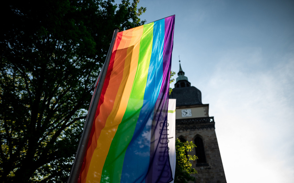 Symbolbild: Eine Regenbogenfahne weht vor einer Kirche.