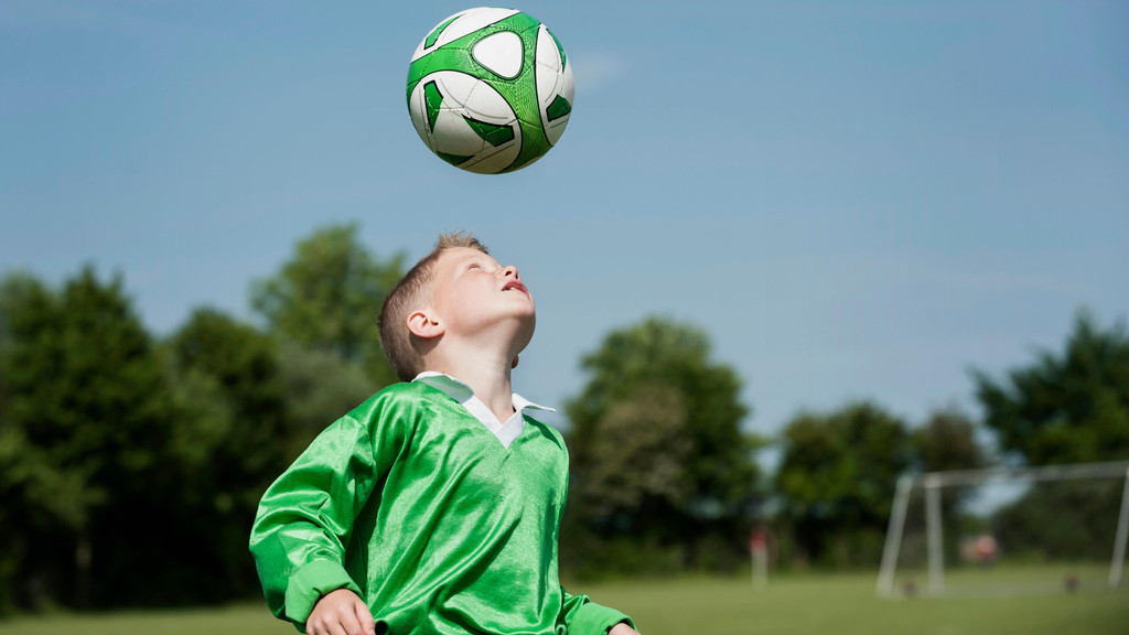 Kind trainiert Kopfbälle mit einem Fußball (Symbolbild)