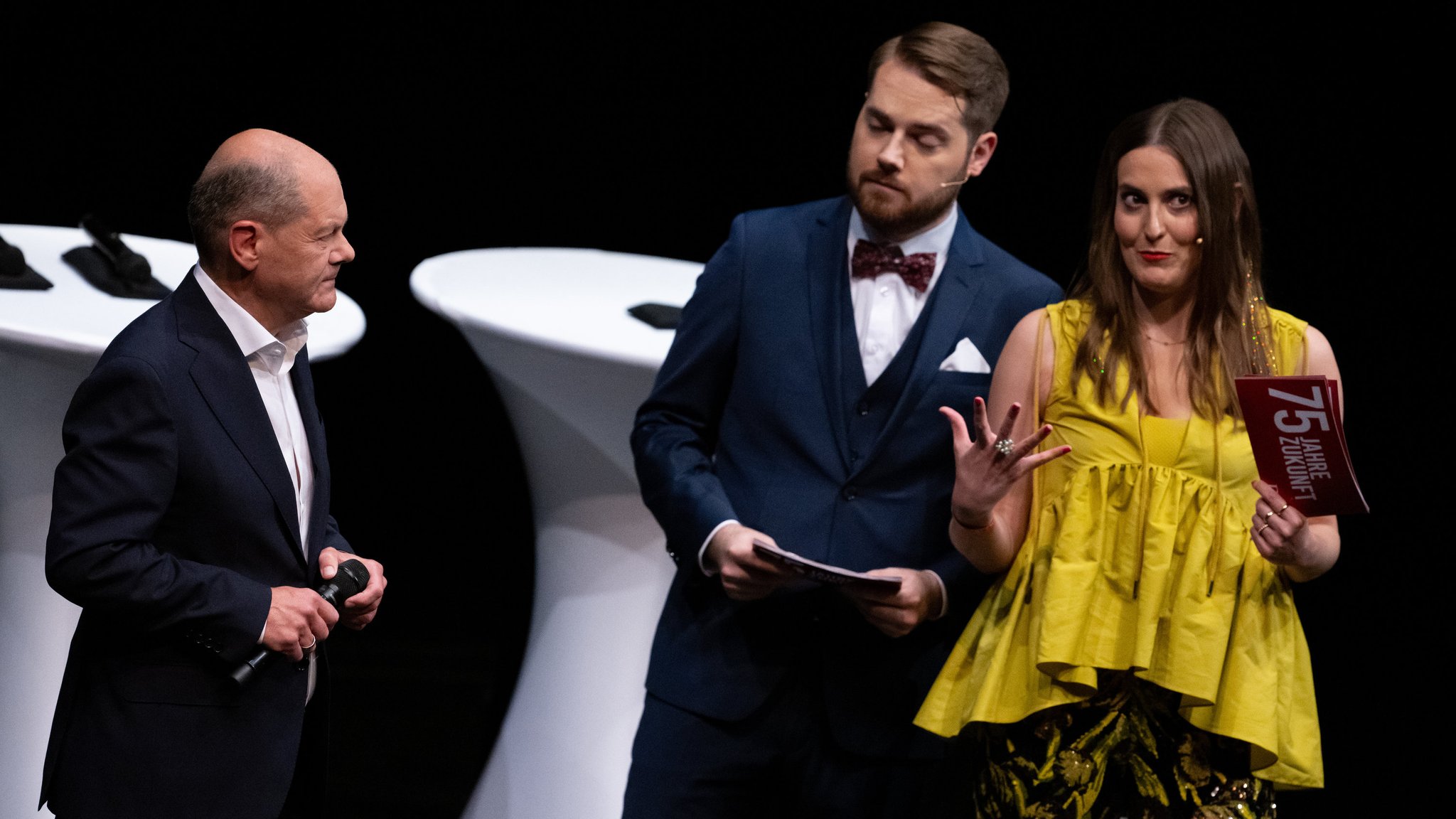 Bundeskanzler Olaf Scholz (SPD, l) spricht mit den Moderatoren Dennis Müller (M) und Lale Ohlrogge bei der 75-Jahr-Feier der Deutschen Journalistenschule (DJS) im Münchner Prinzregententheater.