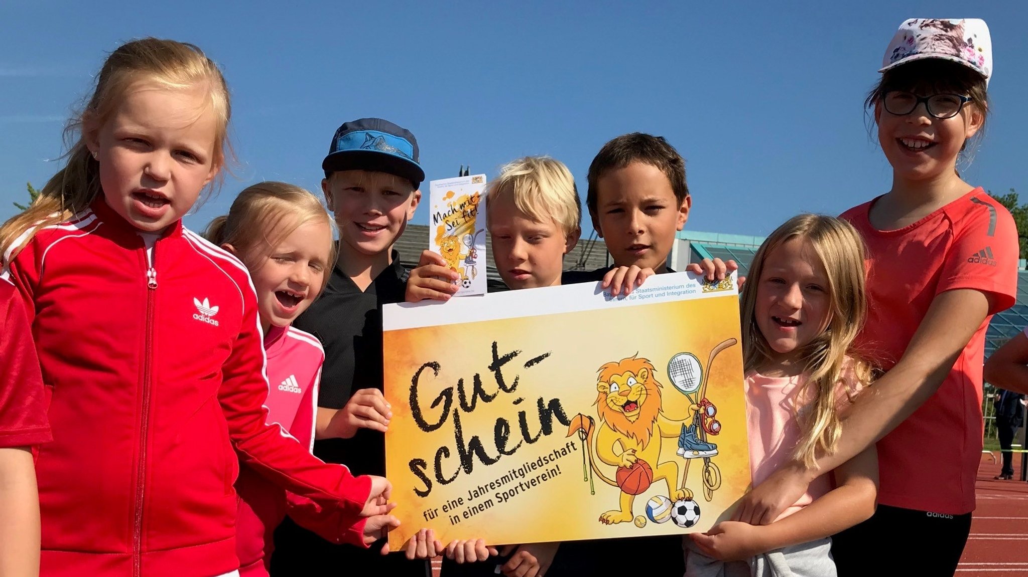 Kinder auf einem Sportplatz halten einen riesigen Gutschein für den Sportverein.