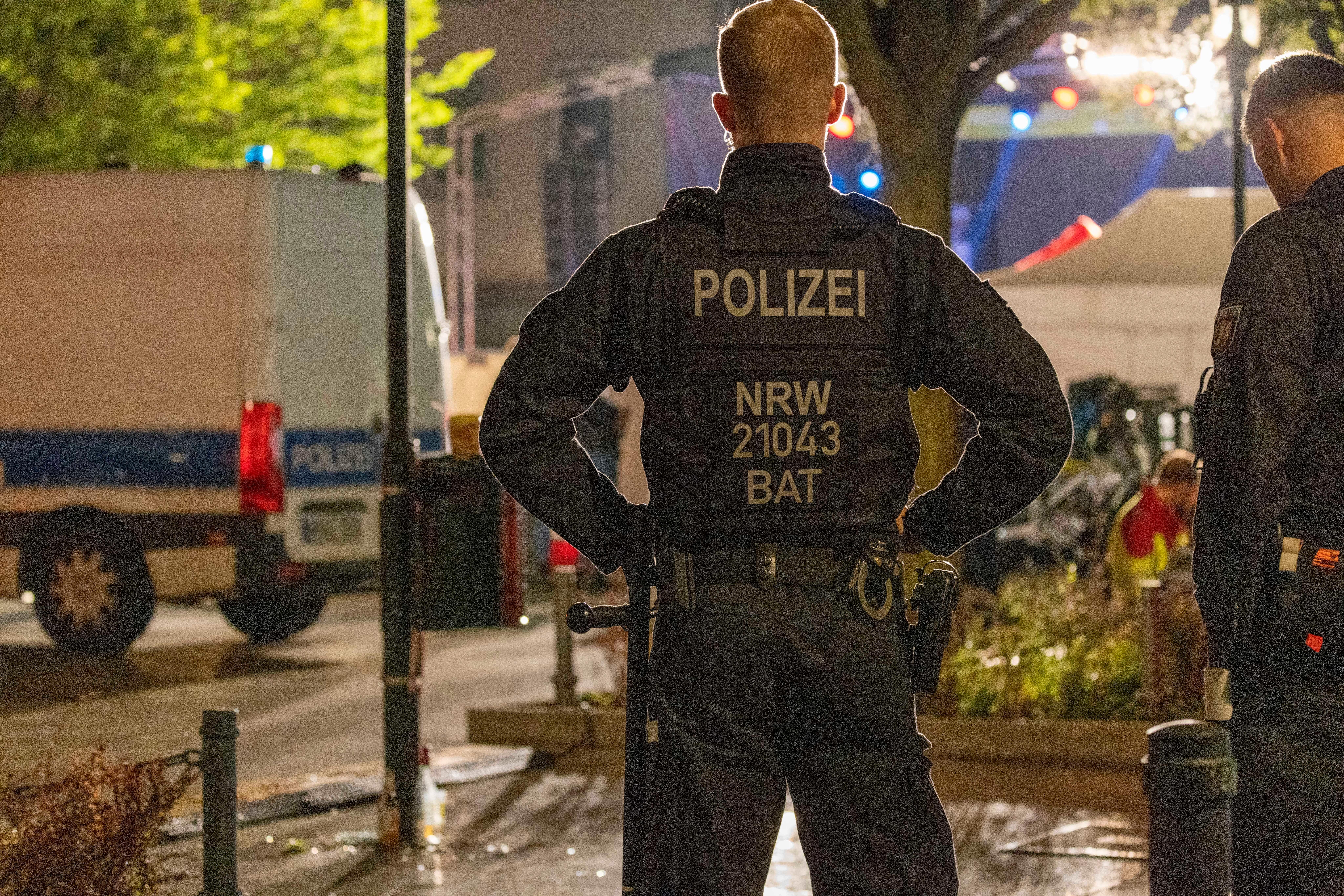 Zwei Polizisten stehen in der Solinger Innenstadt, neben ihnen ein Polizeifahrzeug.