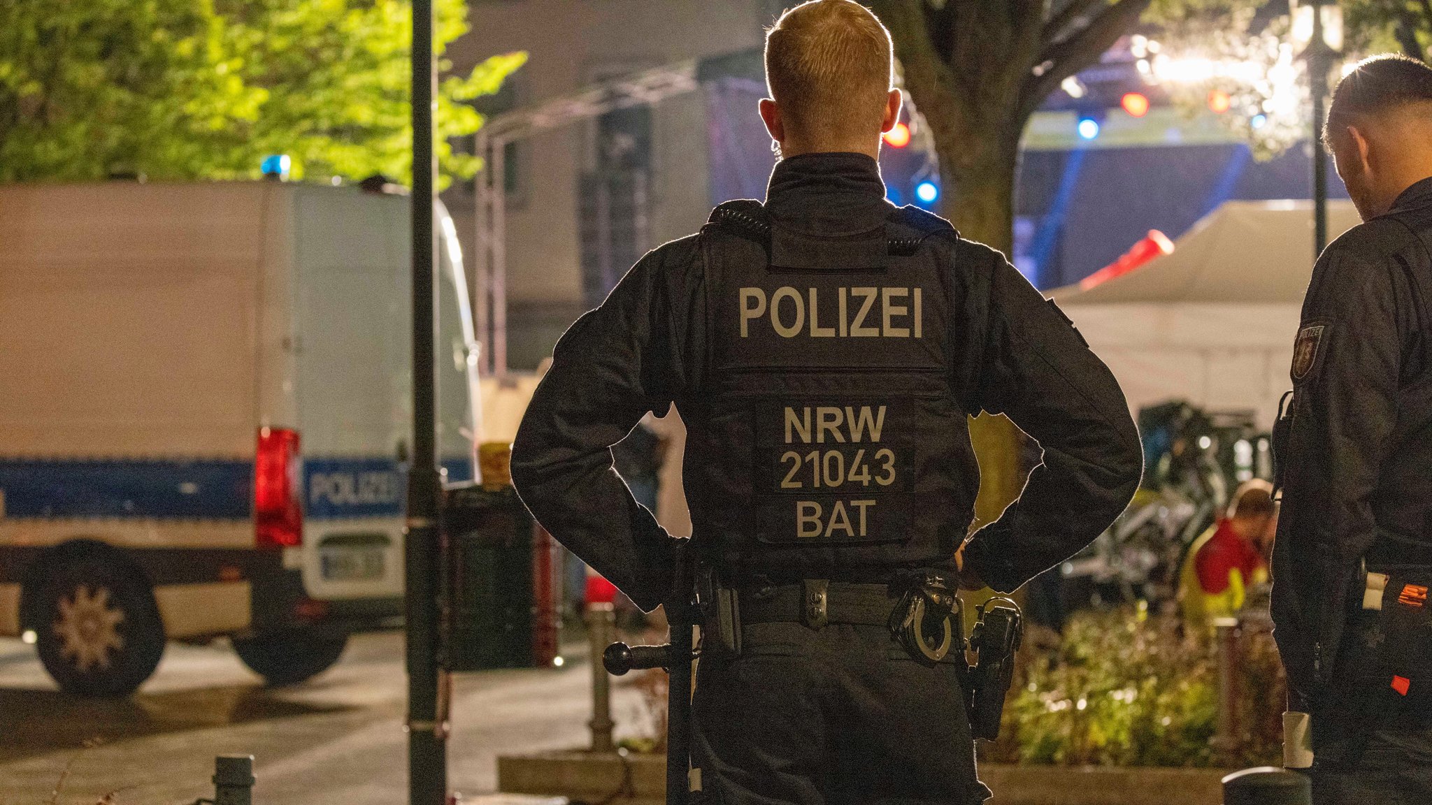 Zwei Polizisten stehen in der Solinger Innenstadt, neben ihnen ein Polizeifahrzeug.